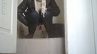 White lady in black coat and pants pisses in the toilet room